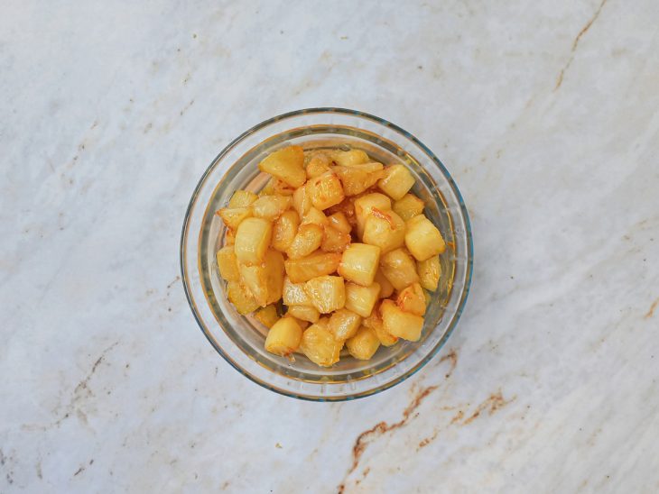 Pedaços de abacaxi reservados num recipiente redondo de vidro.