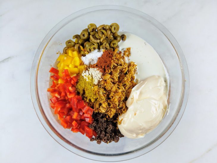 Azeitonas, frango desfiado, pimentões, uva-passas, alho em pó, páprica, sal, lemon pepper, creme de leite e maionese adicionados a tigela com trigo para quibe.