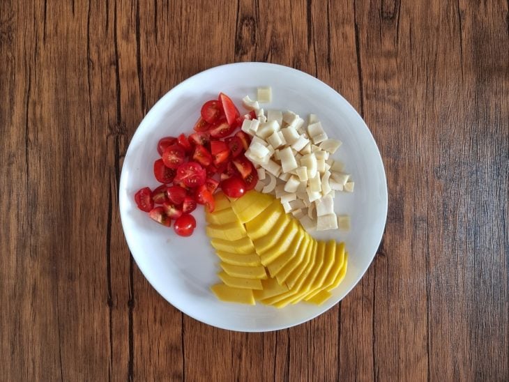 Tomate-cereja, palmito e manga cortados em um prato branco.