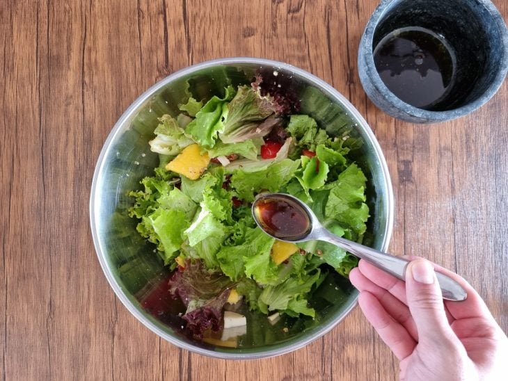 Molho sendo colocado com uma colher sobre as saladas.