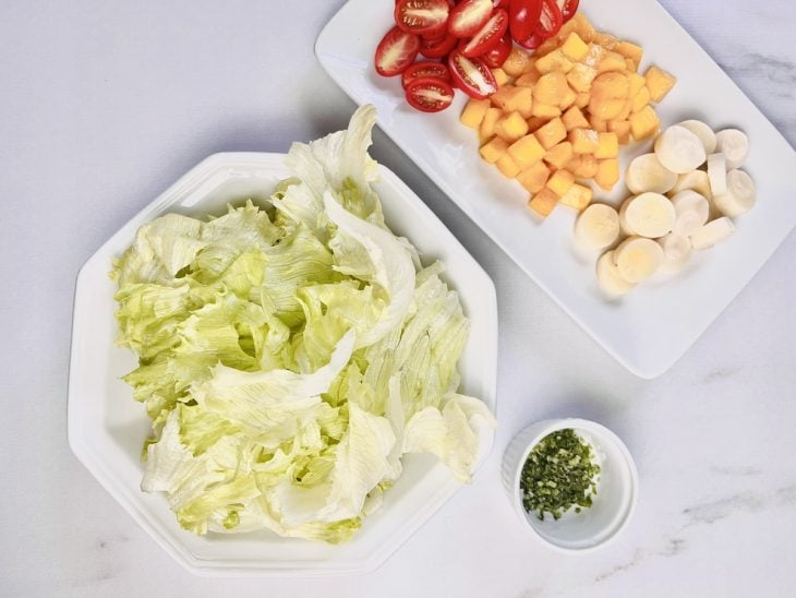 Alface, tomates, palmito, mangas e cebolinha picados sobre uma tábua de cozinha.