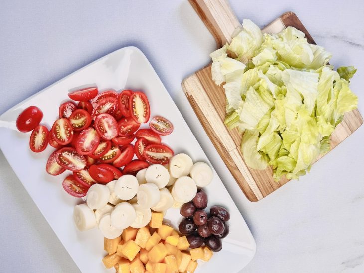 Tomates, palmito, azeitonas, manga e alface picados sobre duas tábuas de cozinha.