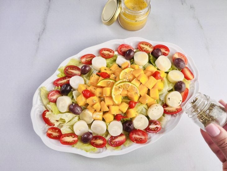 Molho para salada e orégano espalhados sobre a salada.