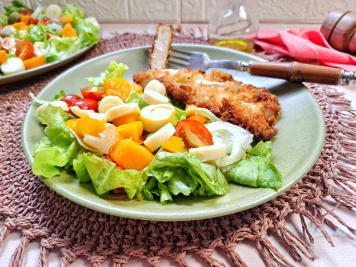Salada tropical simples pronta para consumo e servida acompanhada por filé de frango empanado.