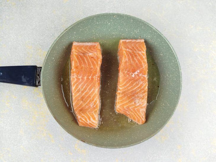 Salmão grelhando com a pele para baixo na frigideira.