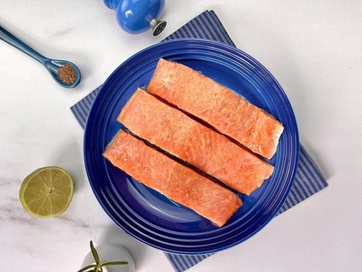Filés de salmão sendo temperadas em um prato.