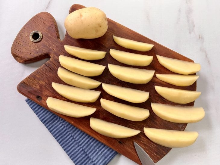 Batatas cortadas em meia-lua em cima de uma tábua.