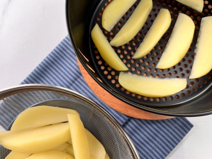 Cesto da airfryer com algumas batatas cozidas.