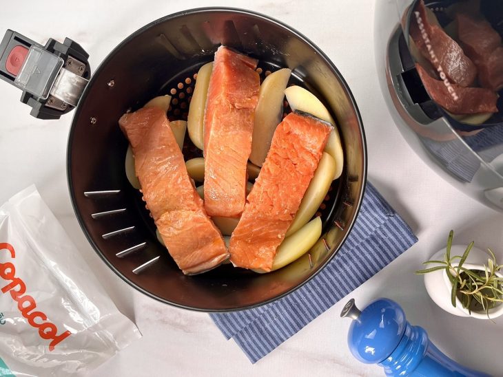 Filés de salmão acomodadas sobre as batatas no cesto da airfryer.