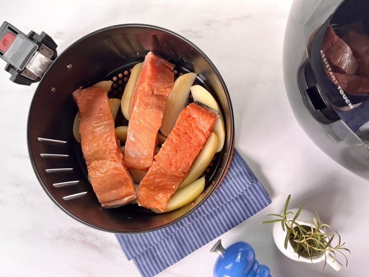 Filés de salmão acomodadas sobre as batatas no cesto da airfryer.