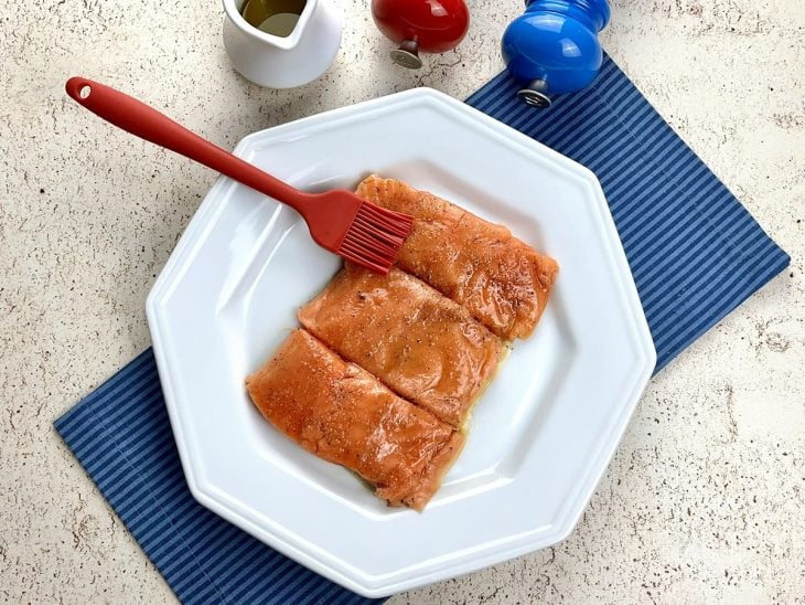Um prato contendo postas de salmão sendo temperados.