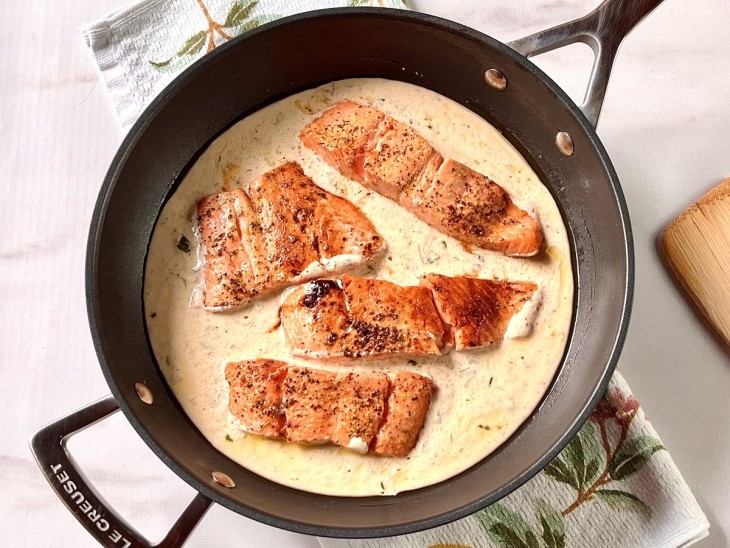 Uma frigideira contendo postas de salmão com molho de creme de leite.