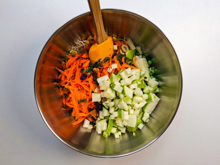 Travessa com frango desfiado recebendo os ingredientes coloridos.