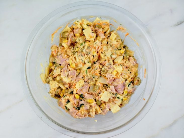 Uma tigela com a mistura do bacalhau refogado, presunto, azeitonas, ervilha, milho, palmito, cenoura, maionese e temperos.