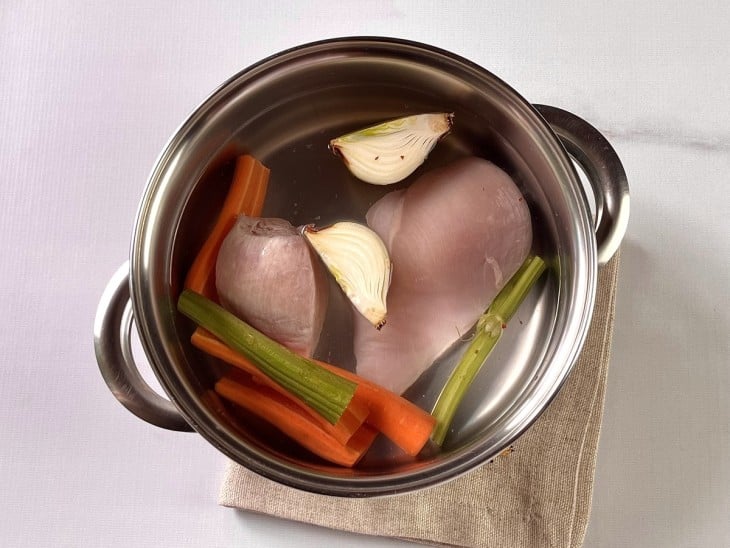 Uma panela contendo peito de frango, talo de salsão, cebola, cenoura e água.