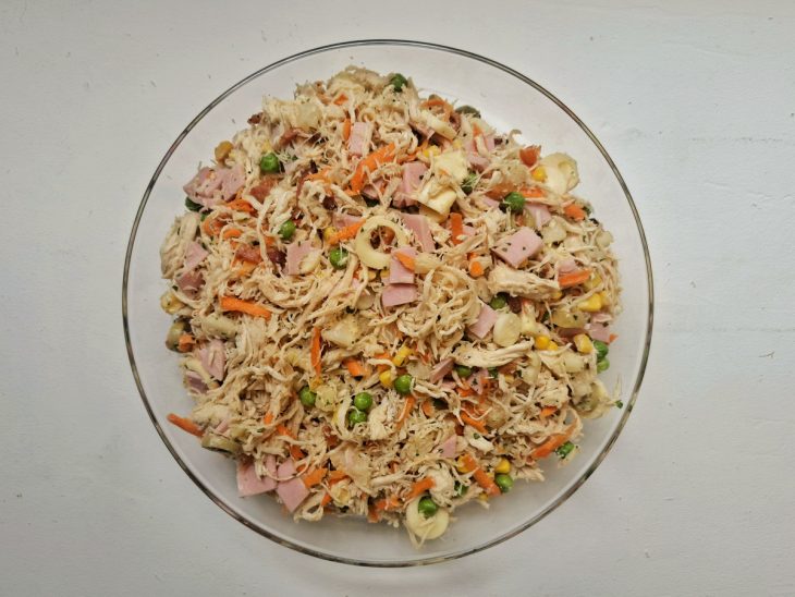 Uma tigela com frango, cenoura, palmito, presunto, abacaxi, ervilha, cebolinha, bacon, azeitonas e milho.