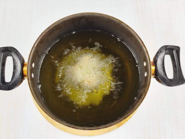 Sambiquiras fritando por imersão em óleo quente, começando a dourar.