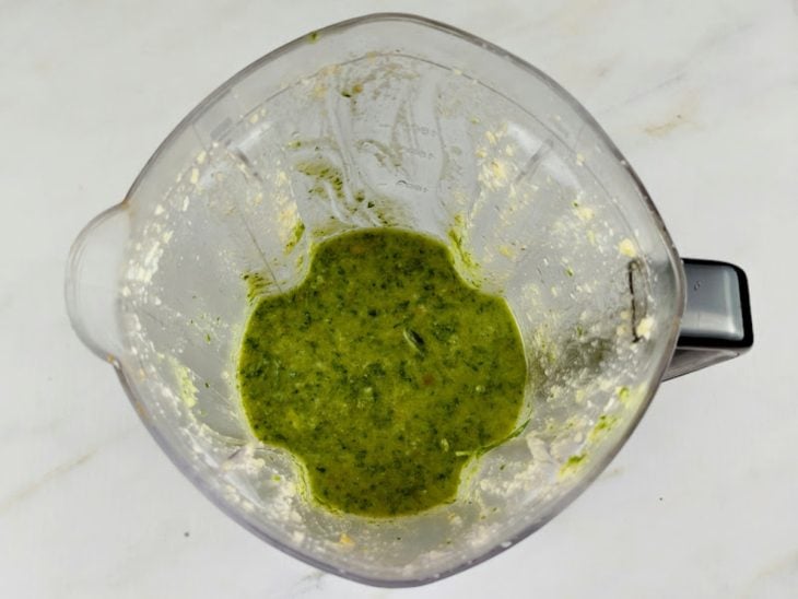 Um liquidificador com os ingredientes do molho pesto batidos.