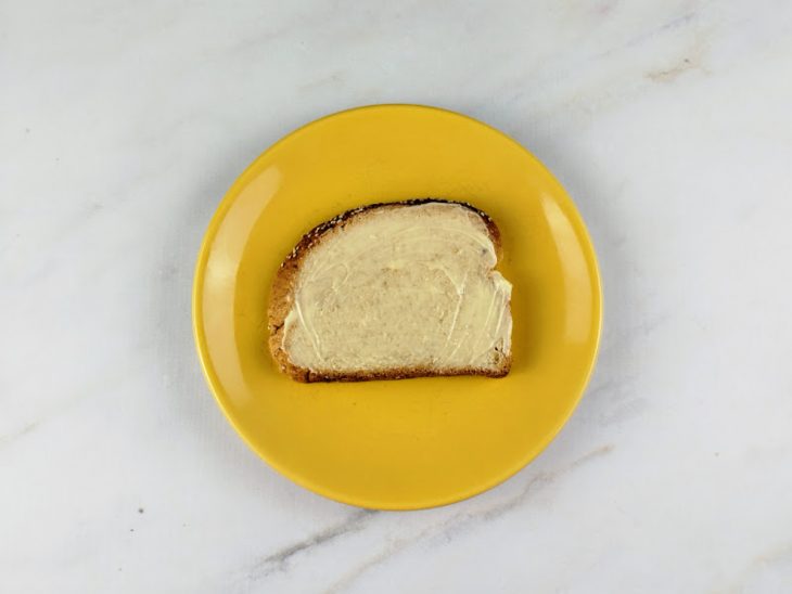 Um prato contendo uma fatia de pão com manteiga.