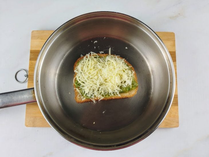 Um prato contendo uma fatia de pão com manteiga, molho pesto e parmesão.