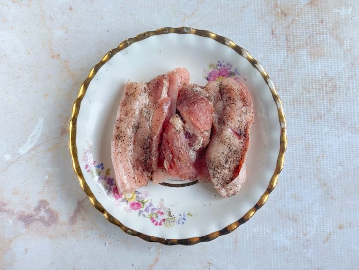 Fatias de panceta temperadas com sal e pimento-do-reino em um prato.