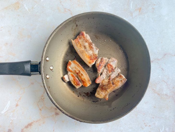 Fatias de panceta fritando em uma panela com manteiga.