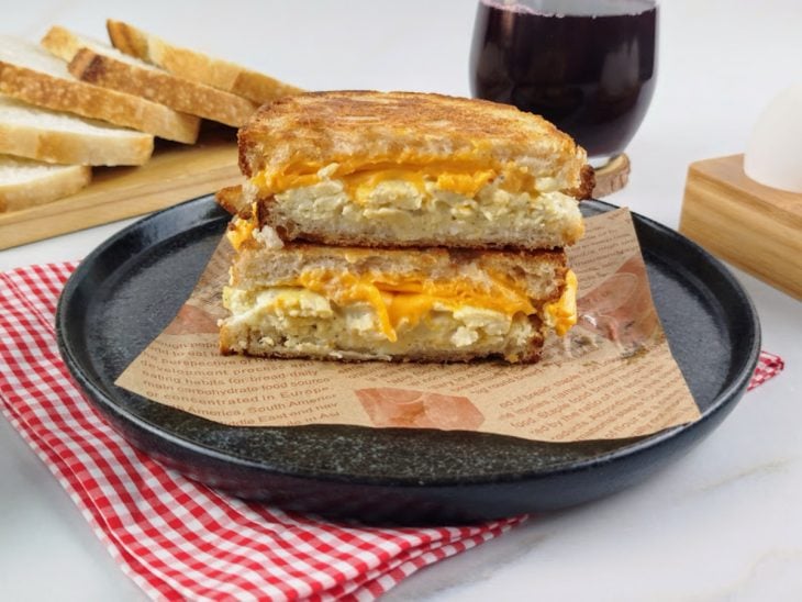 Sanduíche fácil e rápido cortado ao meio em um prato redondo preto e pronto para servir.