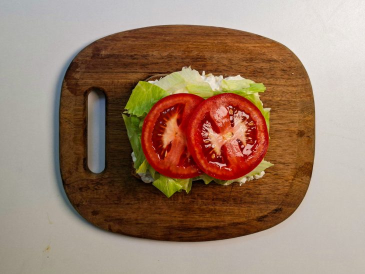 Alface e rodelas de tomate acomodadas sobre o recheio.