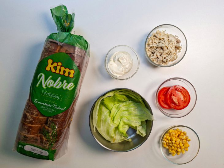 Ingredientes organizados sobre a bancada com pão integral, frango desfiado e vegetais.