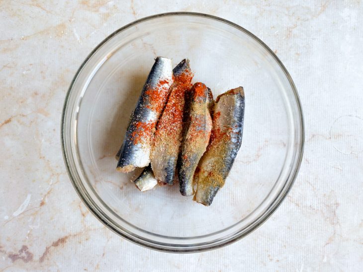 Numa tigela, as sardinhas com com sal, colorau e cominho.
