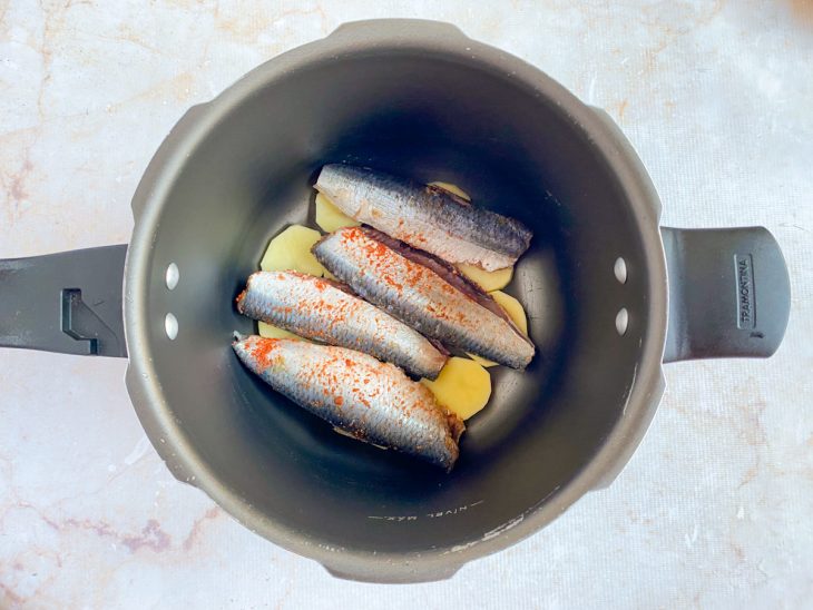 Na panela de pressão, uma camada de batatas, e outra com as sardinhas temperadas.