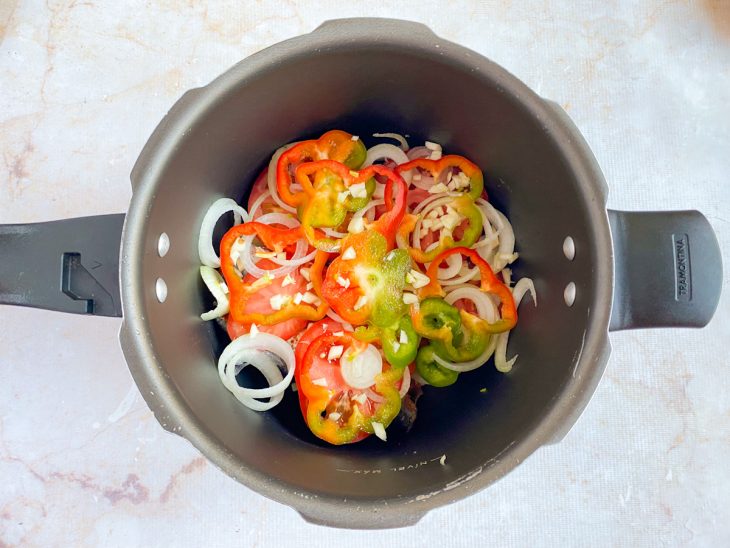Na panela de pressão, por cima da camada de sardinhas, uma camada de tomate, cebola, pimentão e alho.