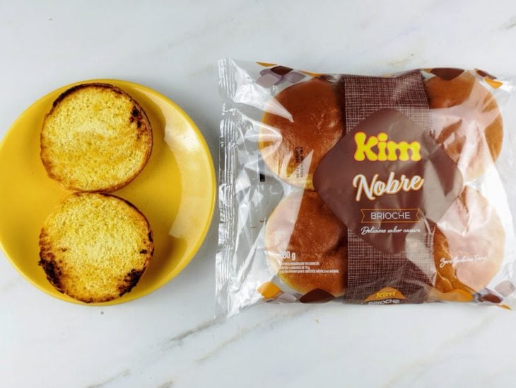 Pão brioche selado na frigideira e reservado em um prato redondo amarelo.