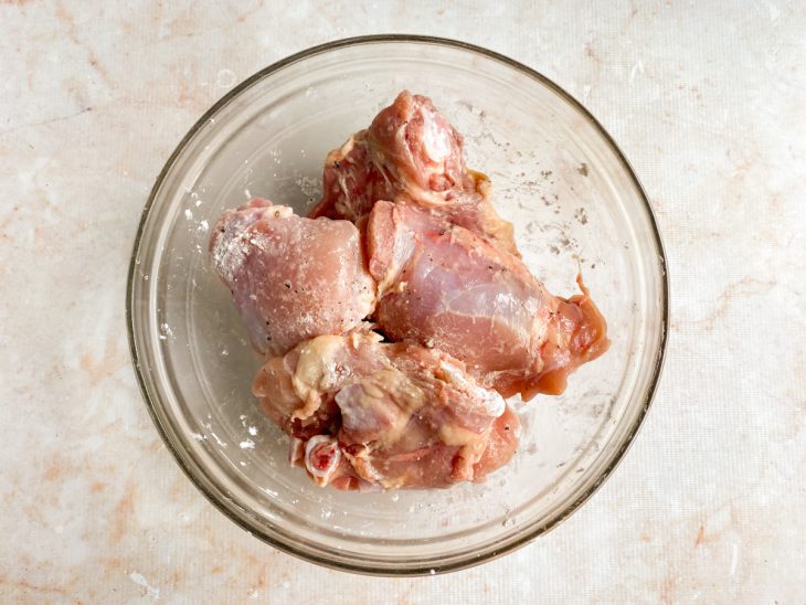 Sobrecoxas temperadas com sal, pimenta-do-reino e amido de milho em uma tigela de vidro.