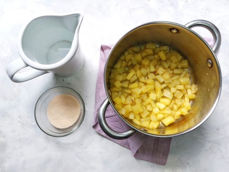 Panela com abacaxi e água e açúcar ao lado.