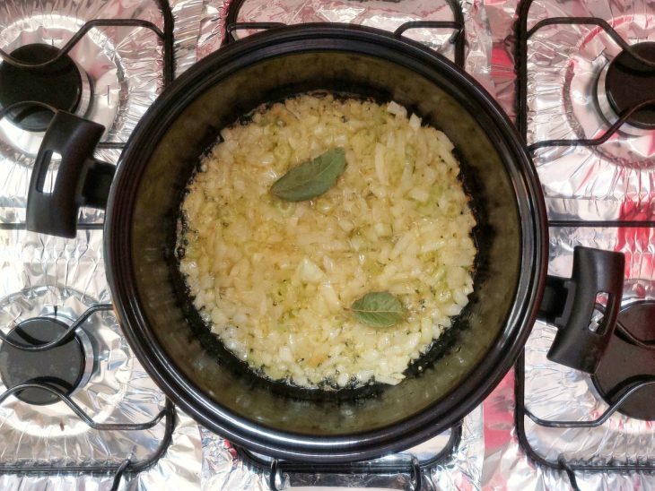 Uma panela com manteiga, azeite, louro, alho, cebola e salsão.