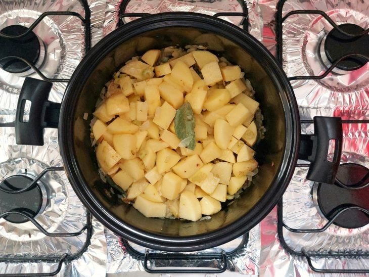 Uma panela com manteiga, azeite, louro, alho, cebola, salsão e batatas.