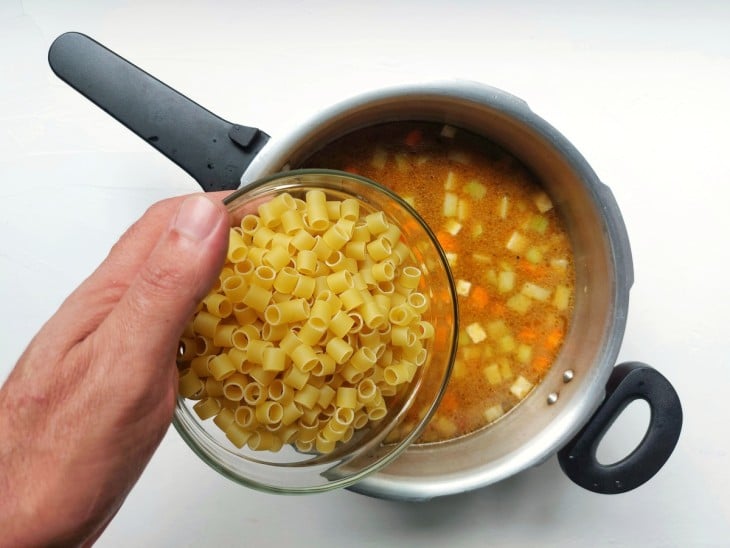 Uma panela de pressão com água, legumes e macarrão.