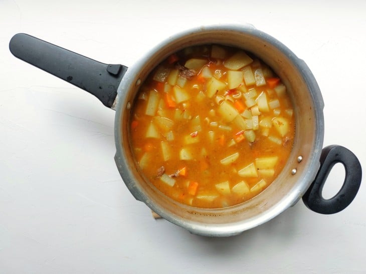 Uma panela de pressão contendo sopa de acém com legumes e macarrão.