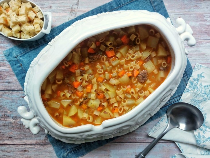 Um recipiente contendo sopa de acém com legumes e macarrão.