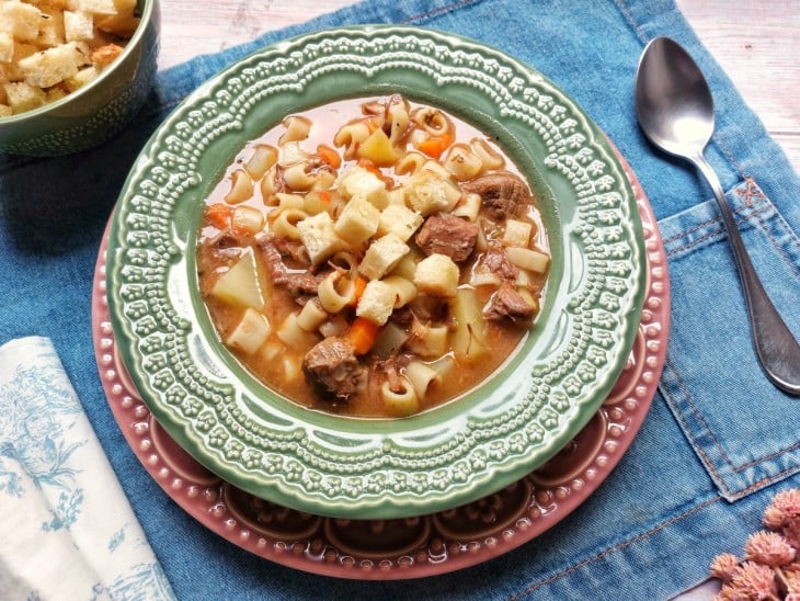 Um prato contendo sopa de acém com legumes e macarrão.