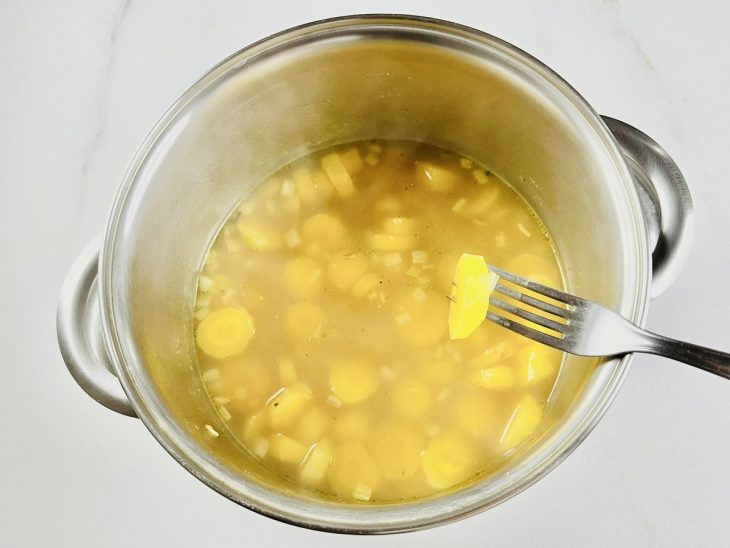 Na panela, garfo espetando umas das rodelas de batata, mostrando o ponto certo.