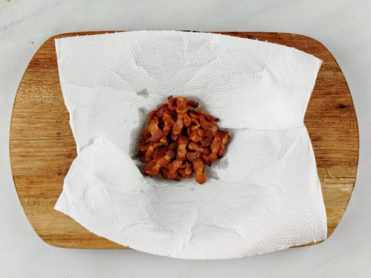 Bacon reservado sobre uma tábua de cozinha forrada com papel-toalha.