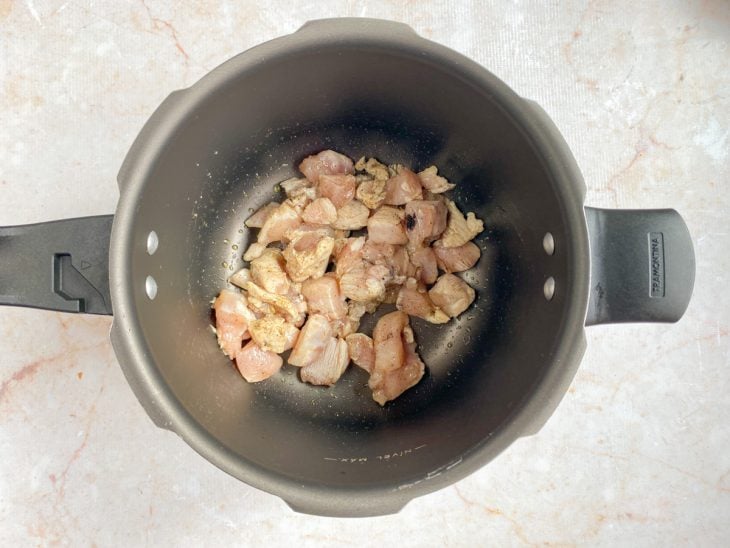 Uma panela de pressão com o frango temperado a dourar.