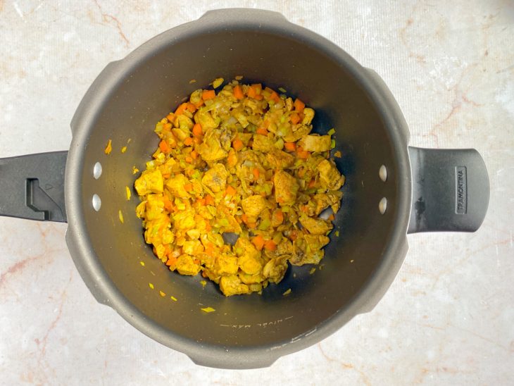 Panela de pressão com o frango, alho, alho-poró, cebola, cenoura e temperos.