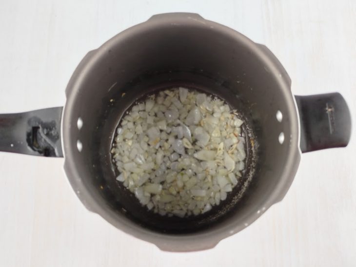 Alho e cebola dourados numa panela de pressão com manteiga.
