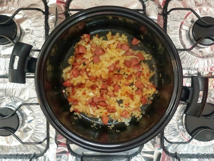 Uma panela com calabresa e temperos refogando.