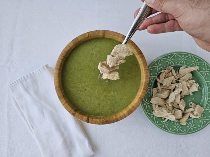 Frango cortado sendo adicionado na tigela com a sopa.