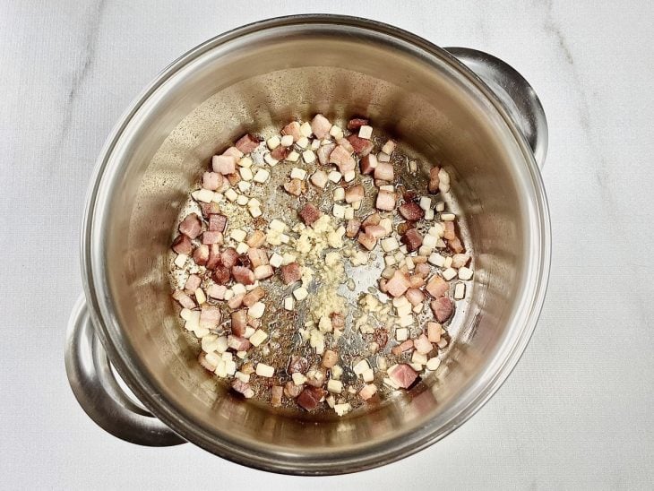 Panela com bacon, alho e cebola a dourar.