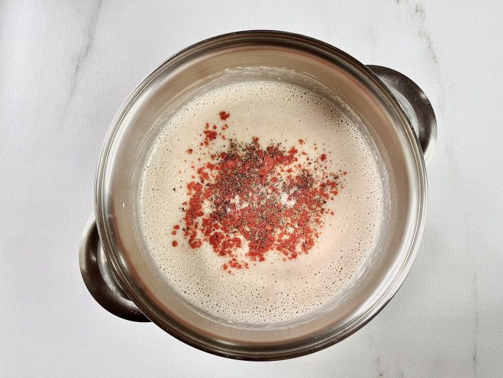 Uma panela com o caldo de feijão, alho, cebola, bacon e temperos.